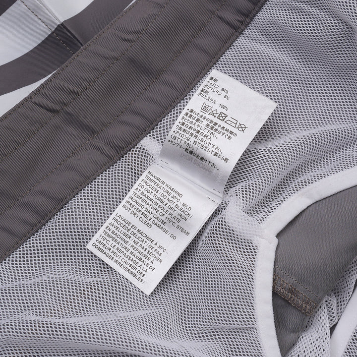 Thom Browne grey board shorts with 4-bar white stripe detail on one leg, red and white braided drawstring waist, and woven logo label at the hem