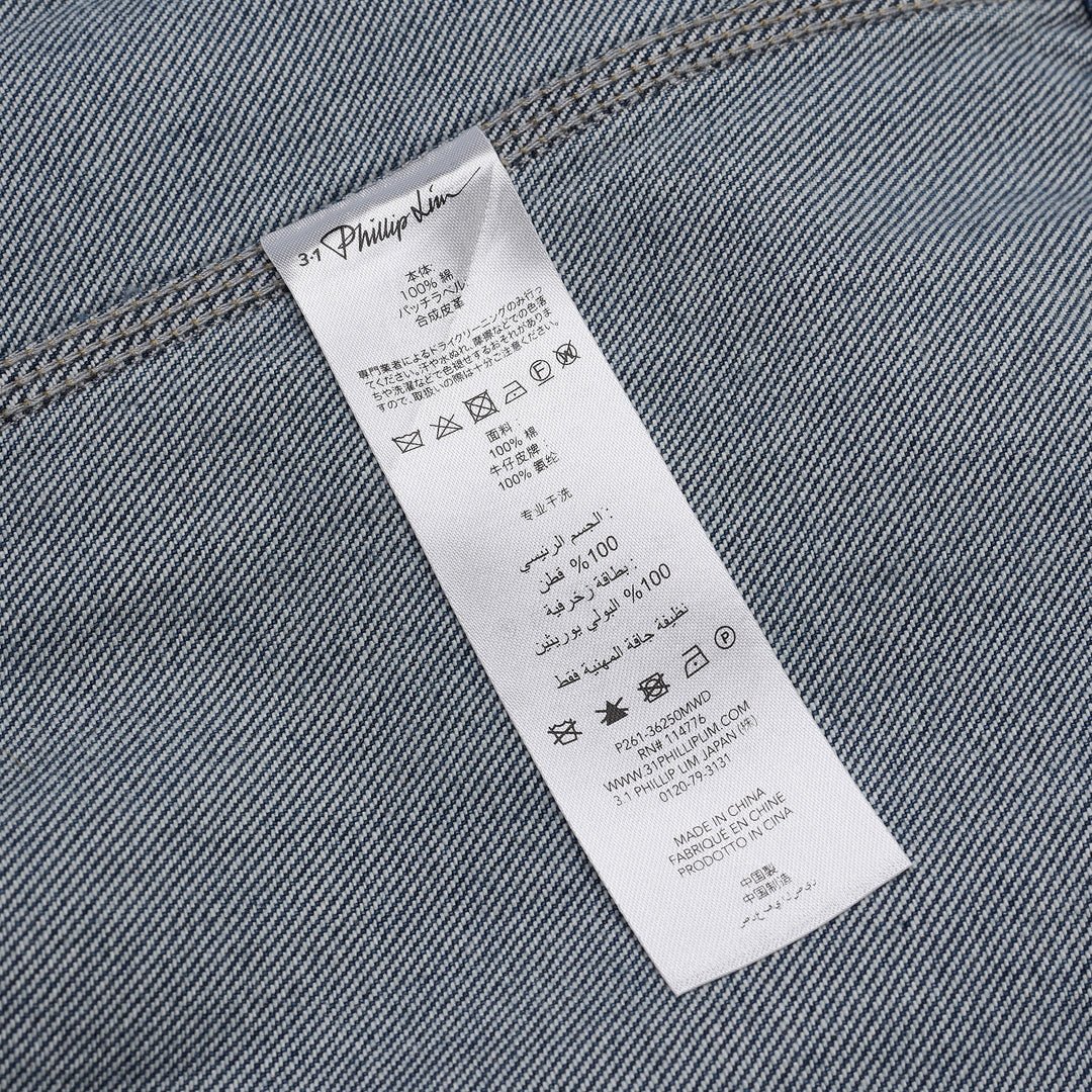 3.1 Phillip Lim mid-wash blue denim asymmetrical midi skirt with diagonal panel seam and A-line flared silhouette, shown on a white background
