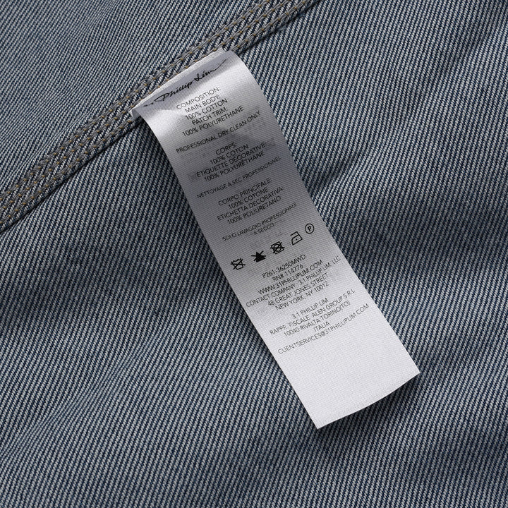 3.1 Phillip Lim mid-wash blue denim asymmetrical midi skirt with diagonal panel seam and A-line flared silhouette, shown on a white background