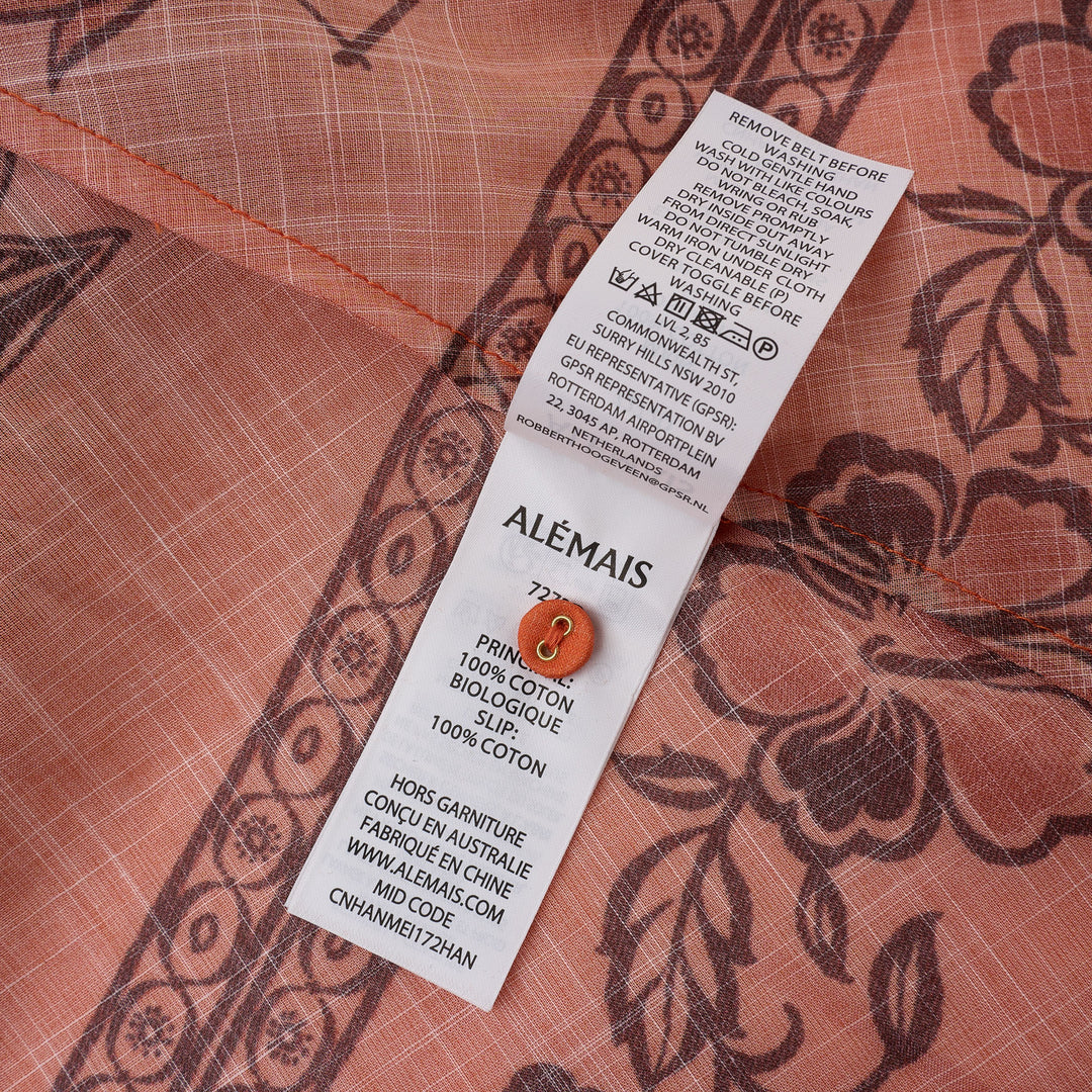 Alemais Boathouse Mini Dress in orange cotton with tropical palm and floral border print, balloon sleeves, gathered neckline with tassel tie, and coordinating rope belt