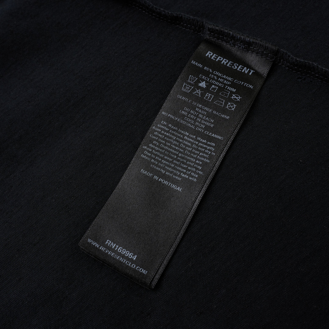 Represent Enemy Tee in washed black, featuring oversized gothic 'Represent' lettering, a hand-drawn lion and diving eagle illustration, blue flame detailing, and 'England' branding on heavyweight cotton
