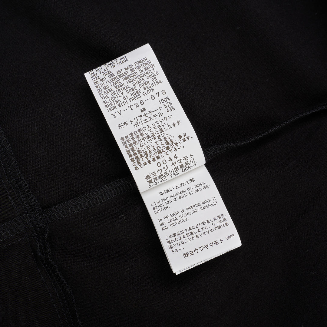 Y's black oversized round neck shirt dress with short folded cuffs, layered T-shirt upper, and buttoned skirt panel, displayed on white background - view 4