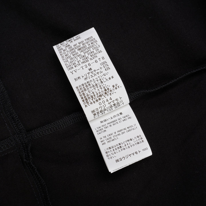 Y's black oversized round neck shirt dress with short folded cuffs, layered T-shirt upper, and buttoned skirt panel, displayed on white background - view 4