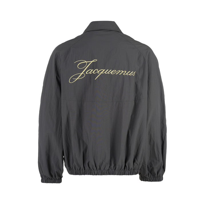 Jacquemus Le Coupe-Vent charcoal grey zip-up windbreaker with collar, elasticated cuffs and hem, and embroidered gold monogram on the chest - view 2