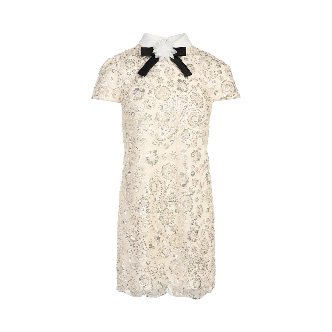 Self-Portrait cream iridescent sequin embellished mini shift dress with white point collar, black grosgrain bow, floral corsage detail, cap sleeves, and scalloped hem