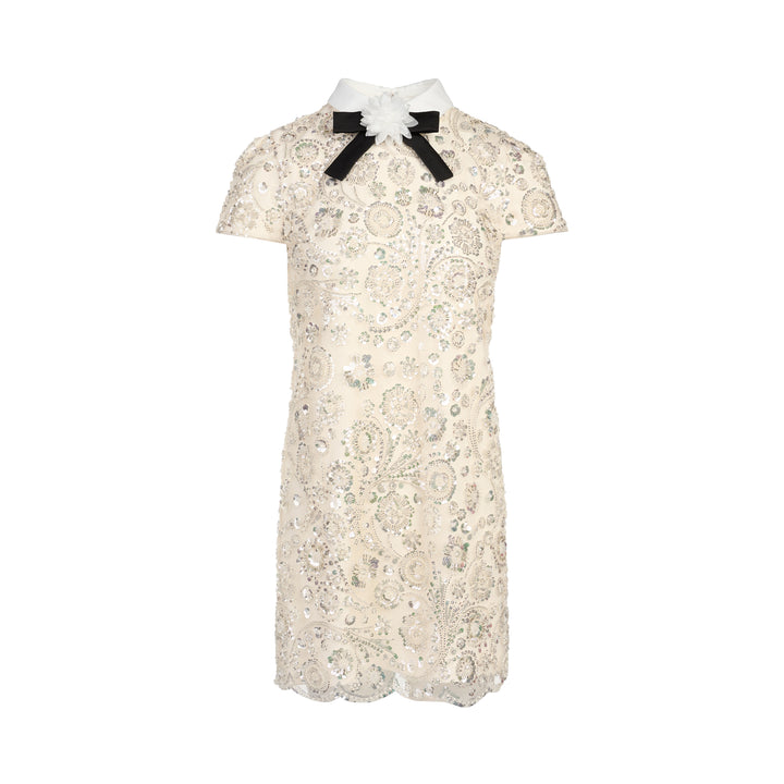 Self-Portrait cream iridescent sequin embellished mini shift dress with white point collar, black grosgrain bow, floral corsage detail, cap sleeves, and scalloped hem