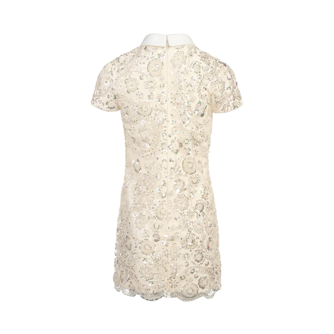 Self-Portrait cream iridescent sequin embellished mini shift dress with white point collar, black grosgrain bow, floral corsage detail, cap sleeves, and scalloped hem