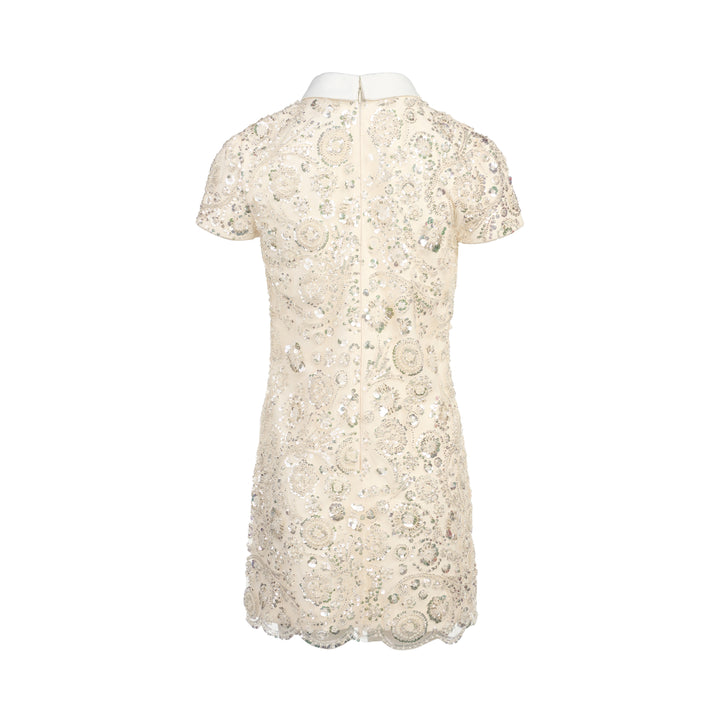 Self-Portrait cream iridescent sequin embellished mini shift dress with white point collar, black grosgrain bow, floral corsage detail, cap sleeves, and scalloped hem