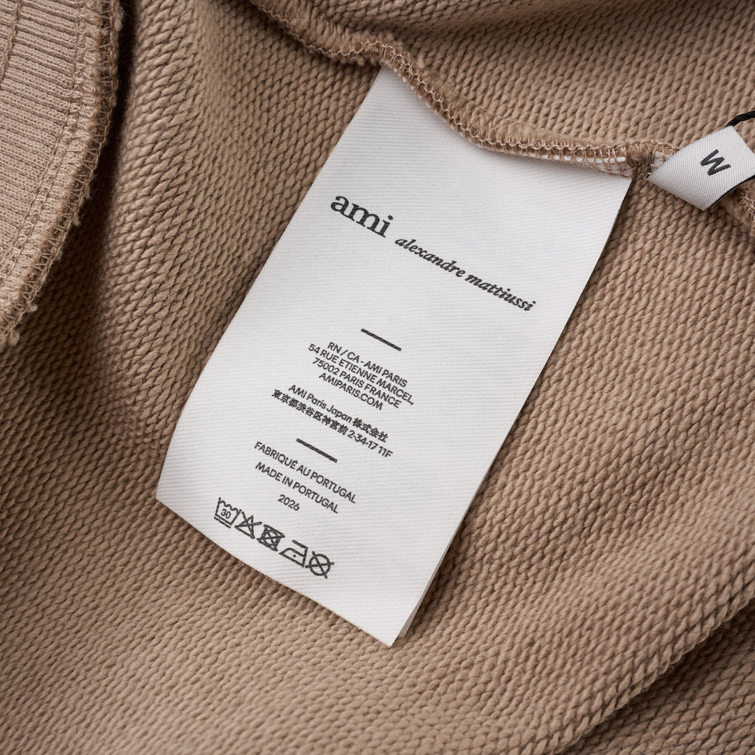 AMI Tonal Emboss Shorts in taupe cotton fleece with drawstring waistband, silver-tone aglets, and subtle logo emboss detail, laid flat on white background