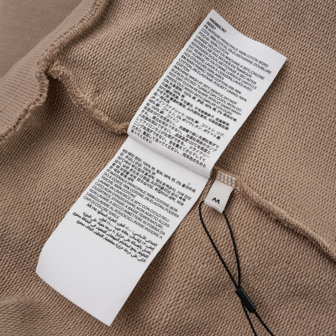 AMI Tonal Emboss Shorts in taupe cotton fleece with drawstring waistband, silver-tone aglets, and subtle logo emboss detail, laid flat on white background