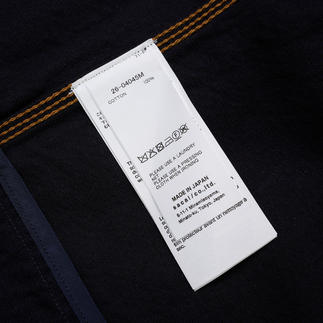 sacai indigo denim trucker jacket with contrast topstitching, pleated front panels, button-flap chest pockets and a layered hem, shown from the front - view 3