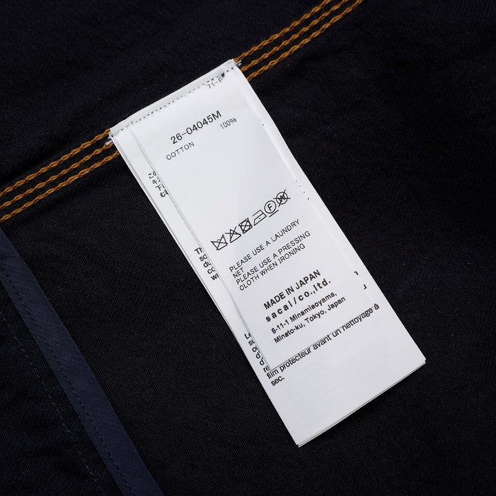 sacai indigo denim trucker jacket with contrast topstitching, pleated front panels, button-flap chest pockets and a layered hem, shown from the front - view 3