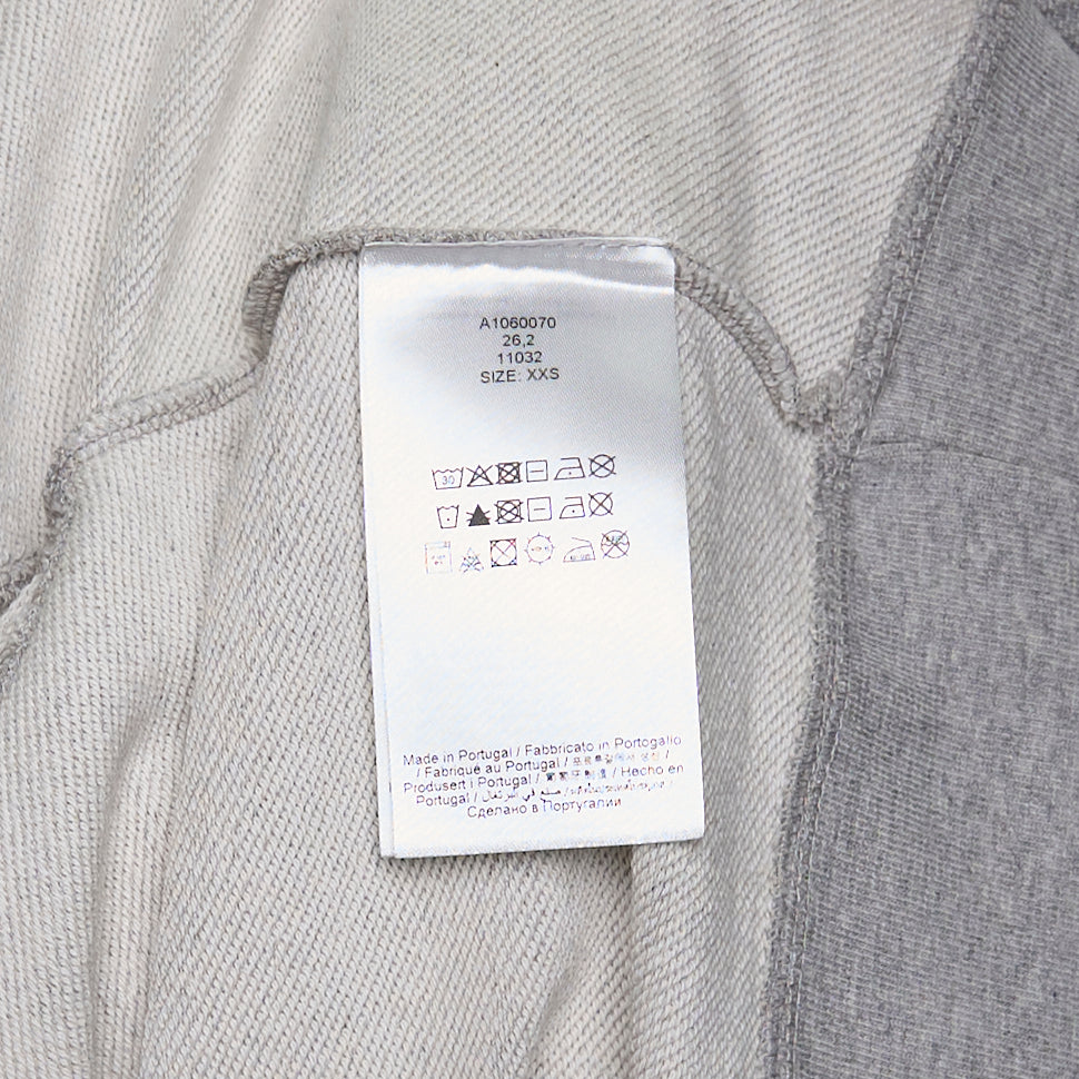 Ganni Isoli Sweater in heather grey marl with white lace frill trim at the hem and cuffs, and an embroidered heart-shaped Ganni logo patch on the chest