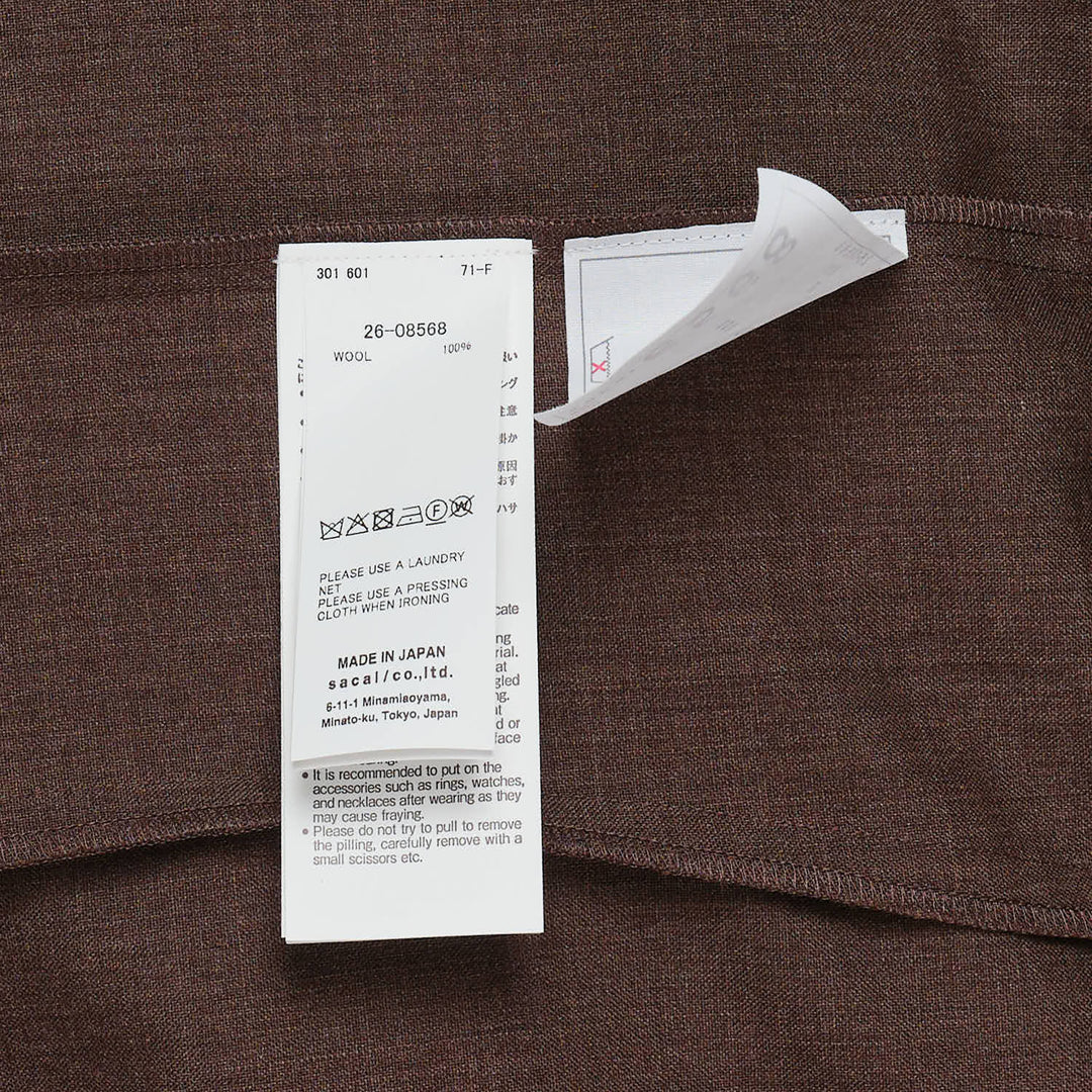 sacai Suiting Short Sleeve Pullover in brown with structured peplum overlay, knife pleats, and contrast navy trim, shown from the back