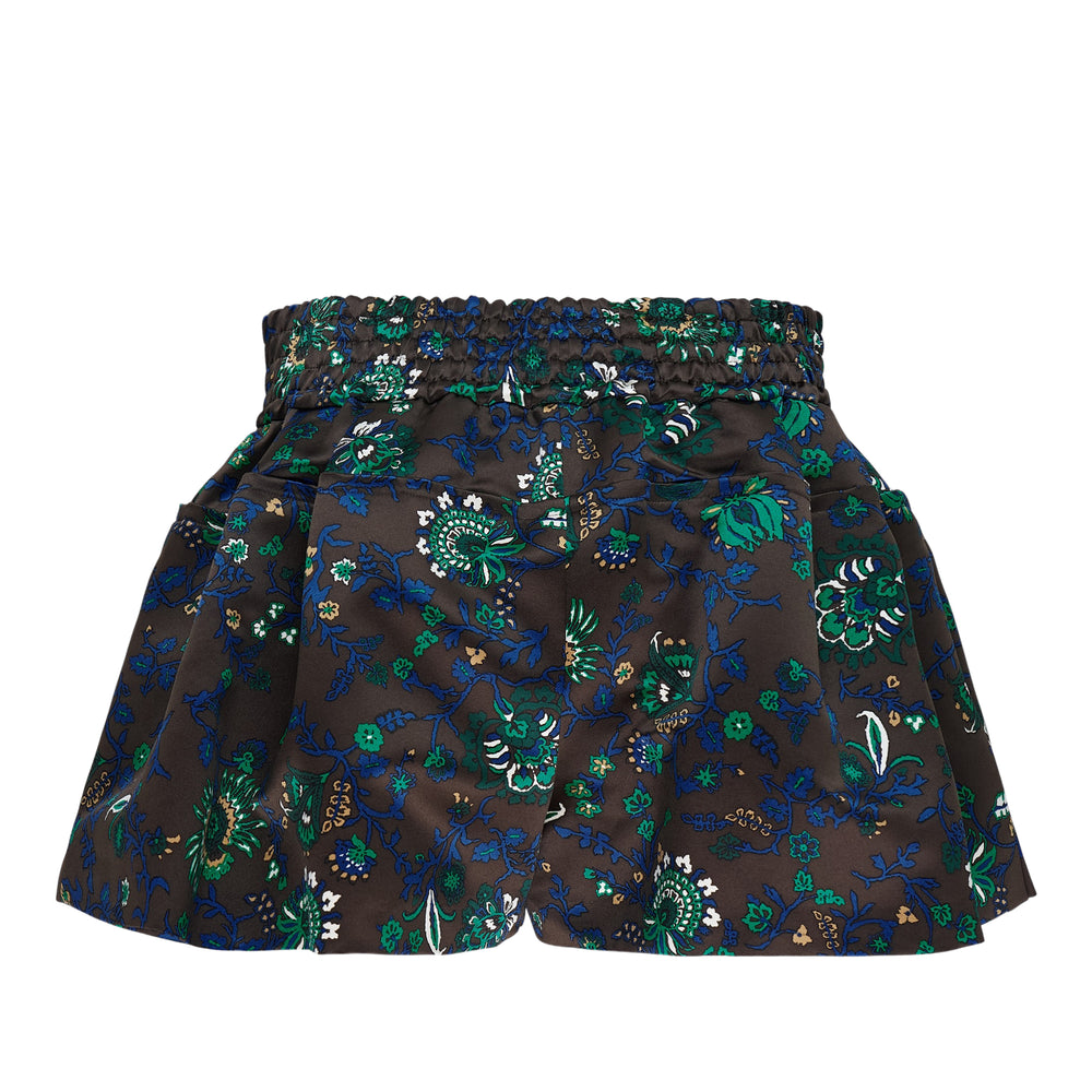sacai Floral Print Shorts in dark satin with green, blue, and gold botanical print, featuring an embroidered branded waistband patch and flared boxing-trunk silhouette