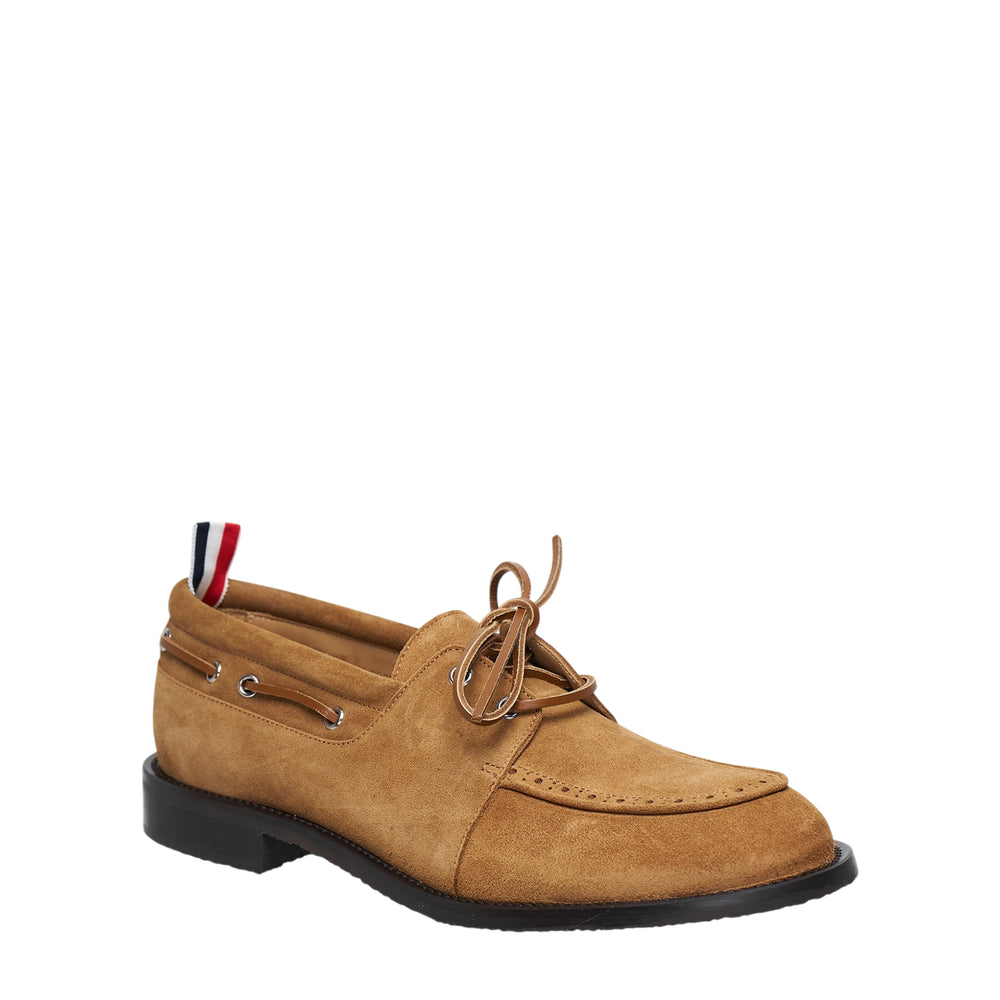Thom Browne dark brown suede padded boat shoe with leather lacing, moccasin toe seam, silver eyelets, and signature red, white, and blue heel tab on a black flexible sole