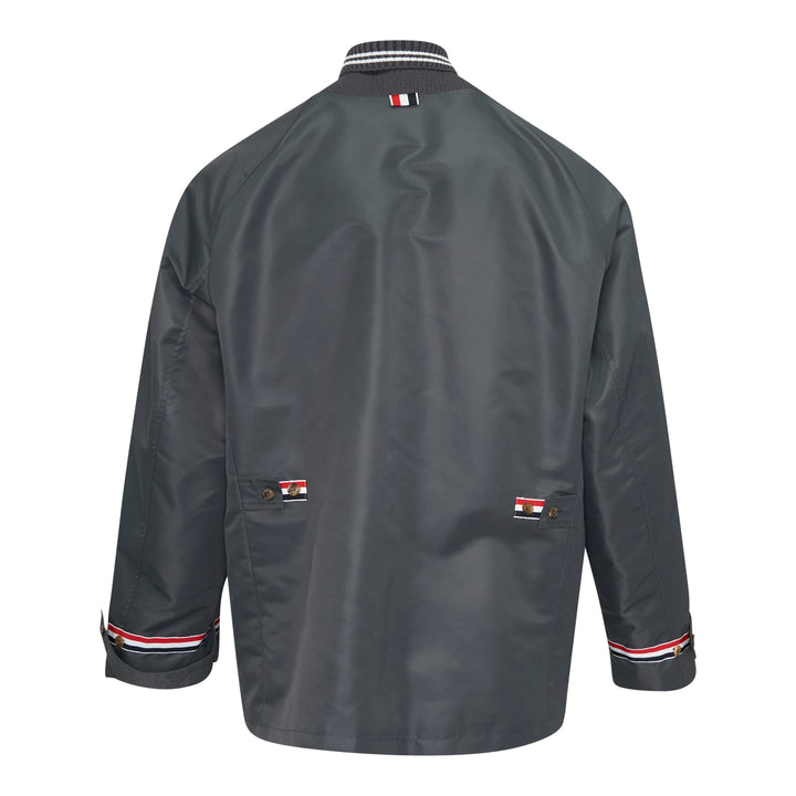 Back view of Thom Browne Cropped Field Jacket in slate grey with ribbed collar, signature red, white, and blue grosgrain trim at collar label, rear pocket tabs, and cuffs
