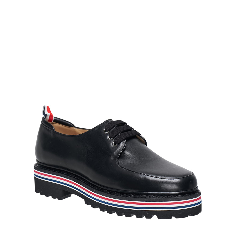 Thom Browne All Terrain Derby in black vitello leather with chunky lug sole featuring signature red, white, and blue striped midsole trim and grosgrain heel tab