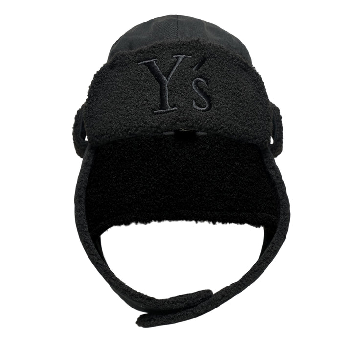 Y's all-black wool trapper hat with sherpa fleece lining, fold-down ear flaps with chin strap, and tonal embroidered Y's logo on the front panel, photographed from the front on a white background.