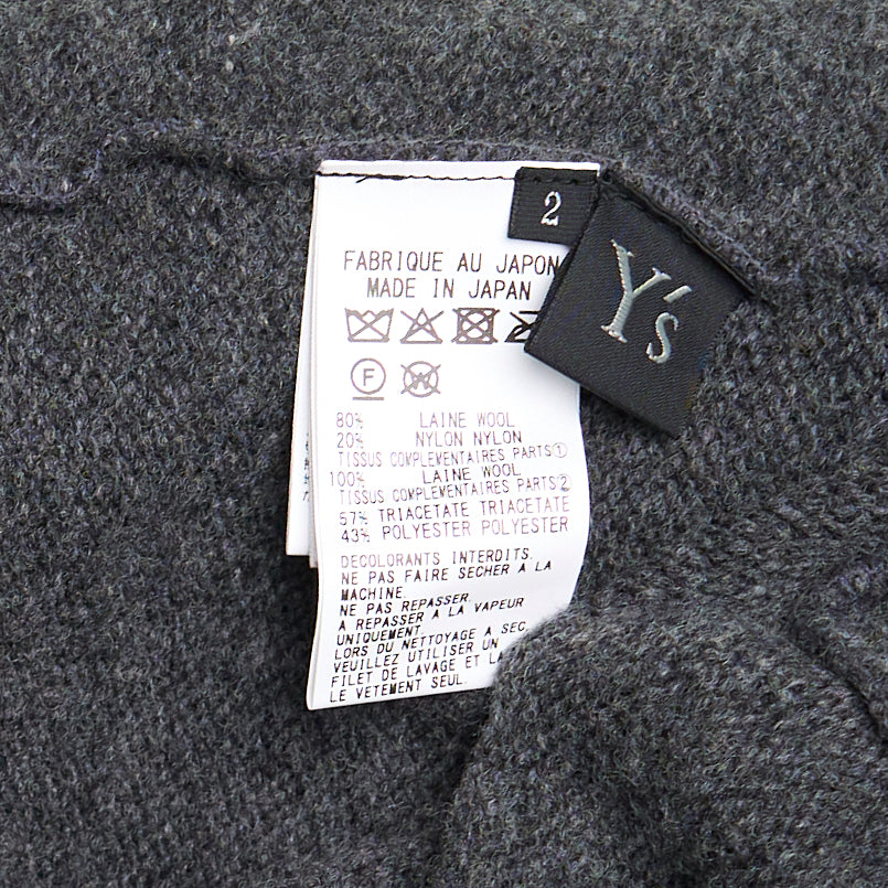Y's Appliqué Short Cardigan in grey marl wool-blend, featuring cascading black mixed-fabric appliqué panels in organza and boucle across the front, with button fastening and ribbed cuffs, back view on white background