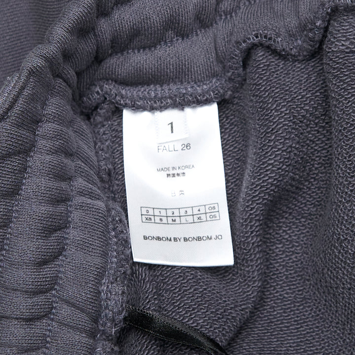 Bonbom Giant Front-Volume Mini Skirt in washed dark navy heavyweight fleece, featuring an elasticated drawstring waistband, belt loop detailing, side patch pocket, and a small woven Bonbom logo label at the lower front