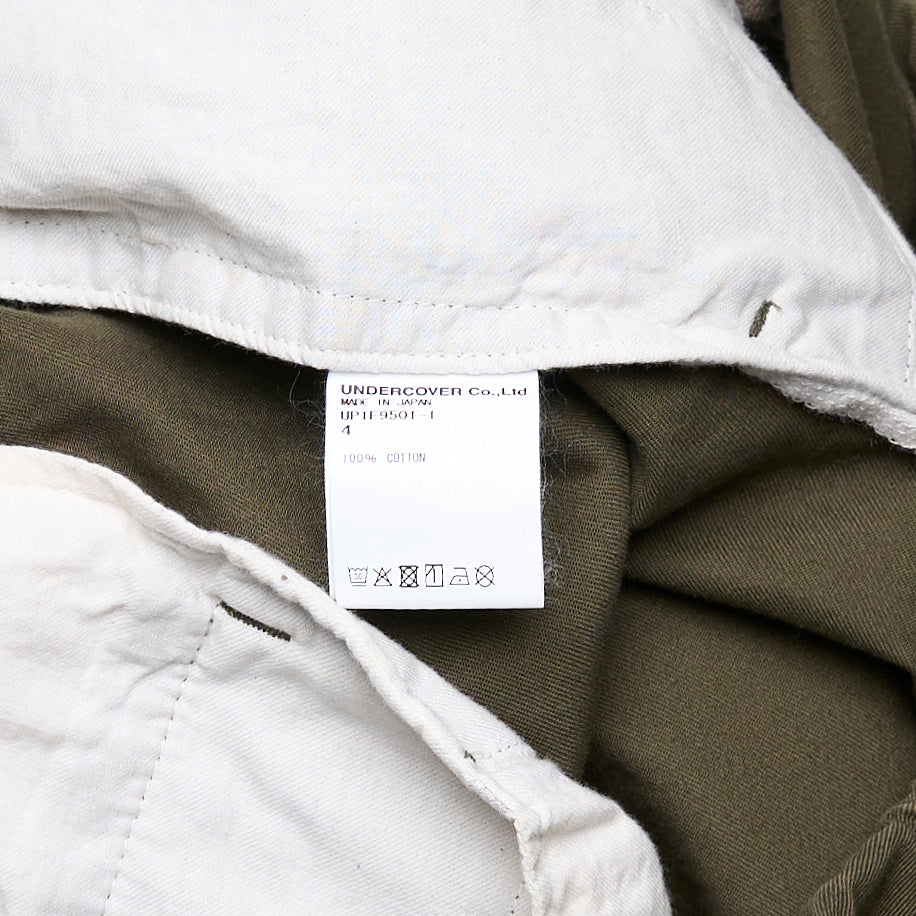 Undercover Witch Hand Elastic Waist Pants in olive green, featuring a tonal black witch claw and serpentine logo graphic on the leg and a concentric spiral drip graphic at the hip, with an elasticated waistband and relaxed wide-leg cut