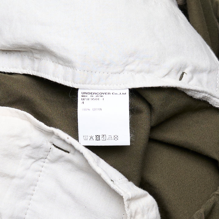 Undercover Witch Hand Elastic Waist Pants in olive green, featuring a tonal black witch claw and serpentine logo graphic on the leg and a concentric spiral drip graphic at the hip, with an elasticated waistband and relaxed wide-leg cut