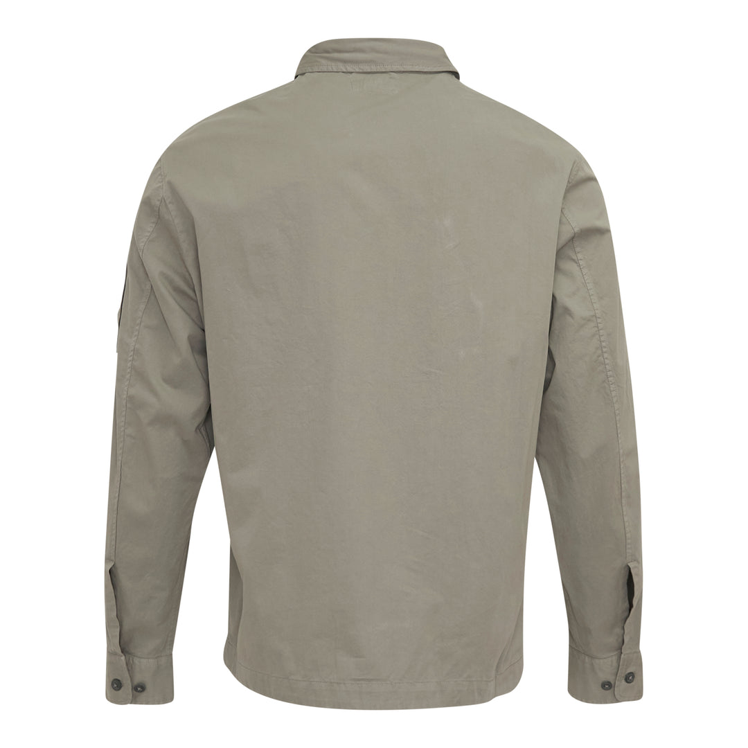 C.P. Company Organic Gabardine Zipped Overshirt in sage green, featuring dual chest flap pockets, concealed zip closure, and signature goggle lens badge on the sleeve