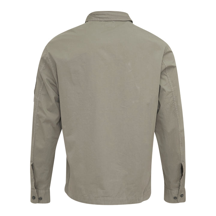 C.P. Company Organic Gabardine Zipped Overshirt in sage green, featuring dual chest flap pockets, concealed zip closure, and signature goggle lens badge on the sleeve