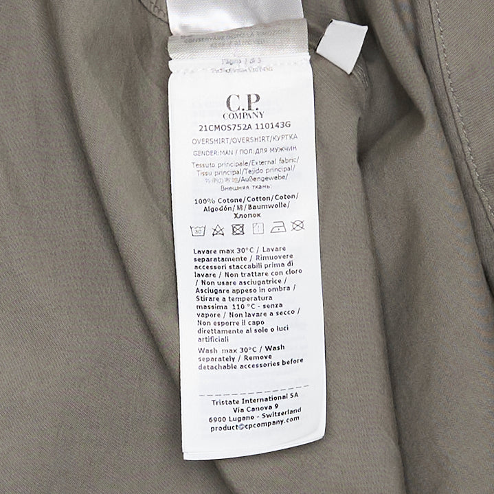 C.P. Company Organic Gabardine Zipped Overshirt in sage green, featuring dual chest flap pockets, concealed zip closure, and signature goggle lens badge on the sleeve