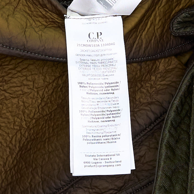 C.P. Company Bi-Face Reversible Jacket in olive coated technical nylon, featuring a stand collar, branded zip fastening, front zip pockets with webbing pulls, and a sleeve lens pocket detail