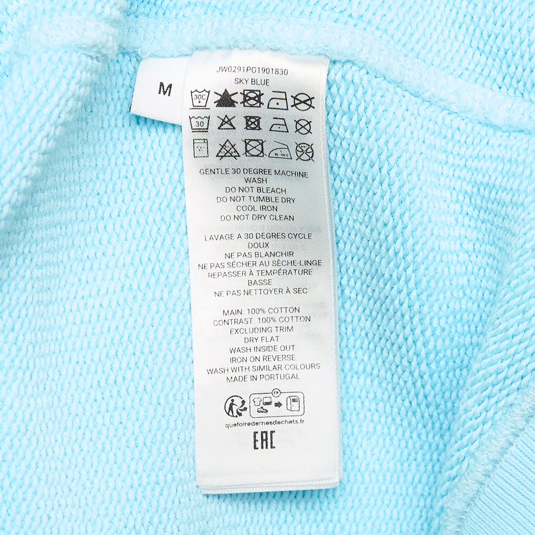 JW Anderson Small Foweles sky-blue crew-neck sweatshirt with dot-matrix embroidered Middle English text and tonal blue grid graphic on the chest, shown flat on a white background