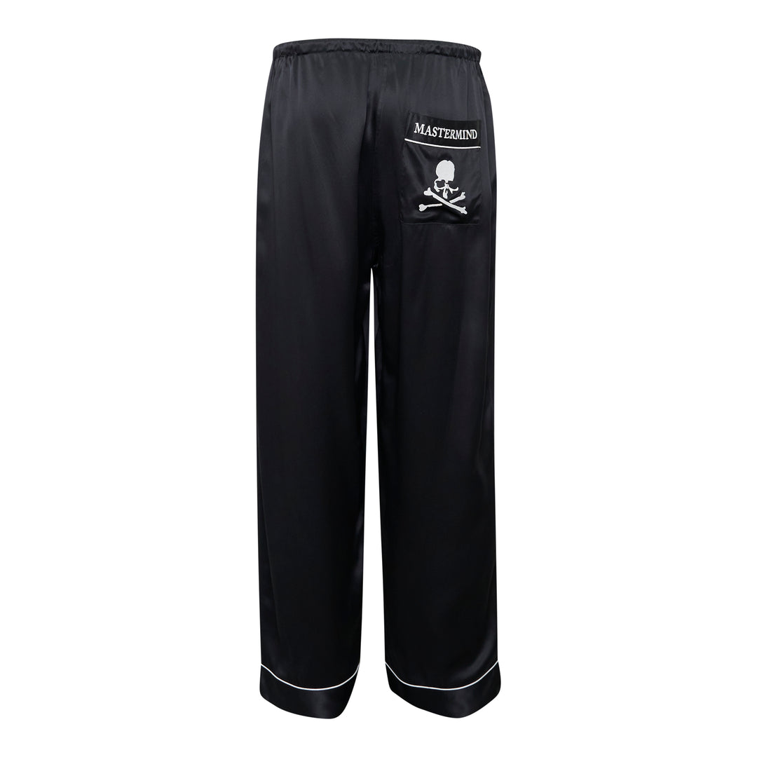 Mastermind black satin pajama set with skull and crossbones embroidery on the chest pocket, white contrast piping trim, button-front long-sleeve top, and relaxed wide-leg trousers