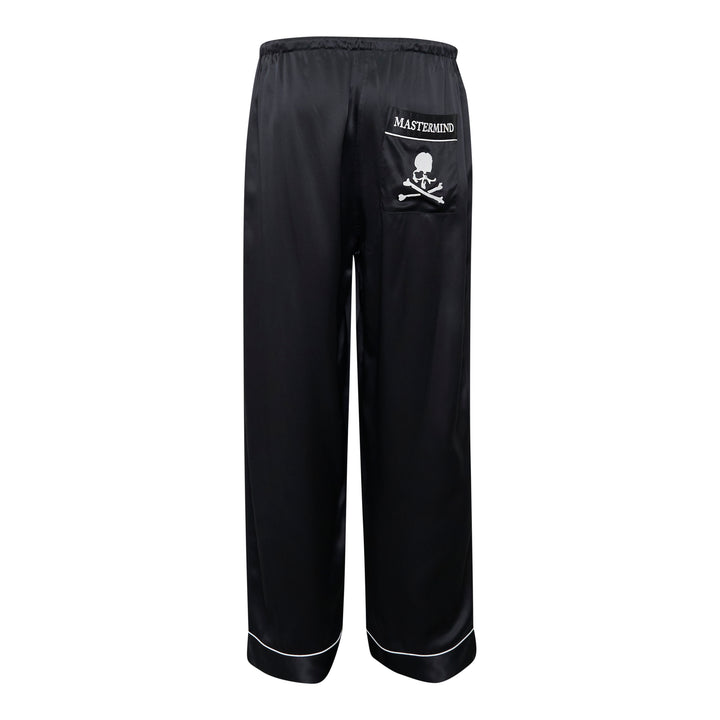 Mastermind black satin pajama set with skull and crossbones embroidery on the chest pocket, white contrast piping trim, button-front long-sleeve top, and relaxed wide-leg trousers