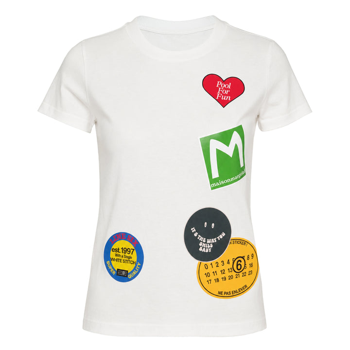 MM6 Maison Margiela white heavy cotton jersey tee featuring playful sticker-style printed graphics including a green MM6 logo, red heart, black smiley circle, vintage badge, and numbered label motifs