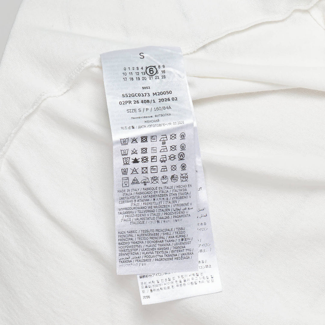 MM6 Maison Margiela white heavy cotton jersey tee featuring playful sticker-style printed graphics including a green MM6 logo, red heart, black smiley circle, vintage badge, and numbered label motifs