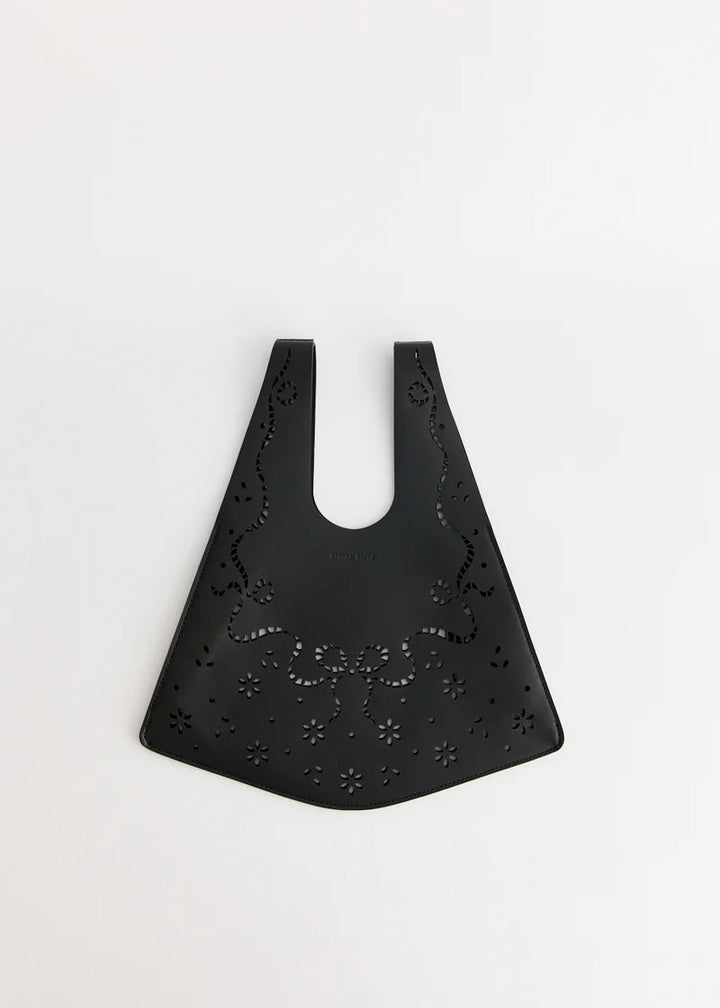 Simone Rocha mini shopper bag in black leather with lasercut lace-inspired bow and floral cutouts, shown flat against a white background