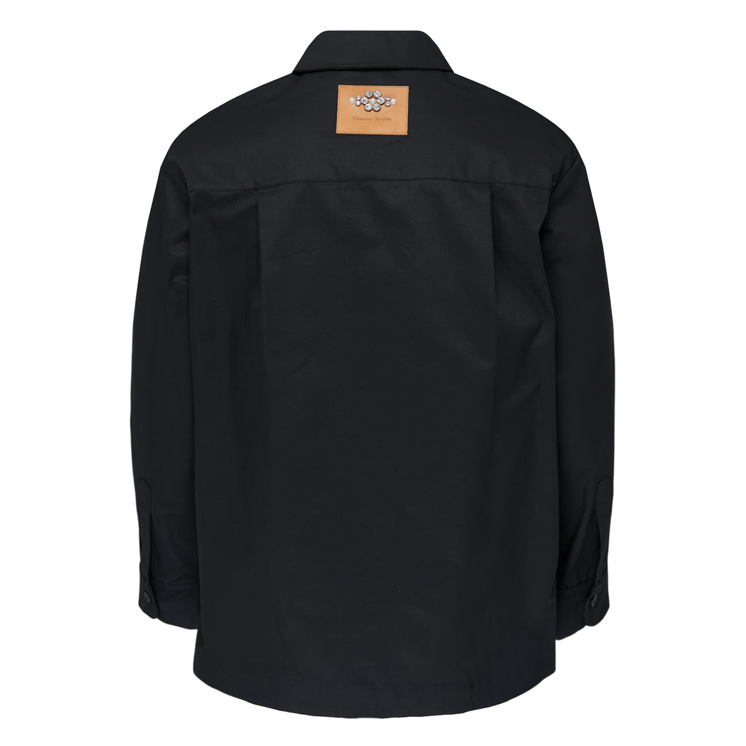 Simone Rocha black cotton twill military overshirt, front view, featuring dual flap chest pockets, tonal button-front closure, and a relaxed oversized silhouette