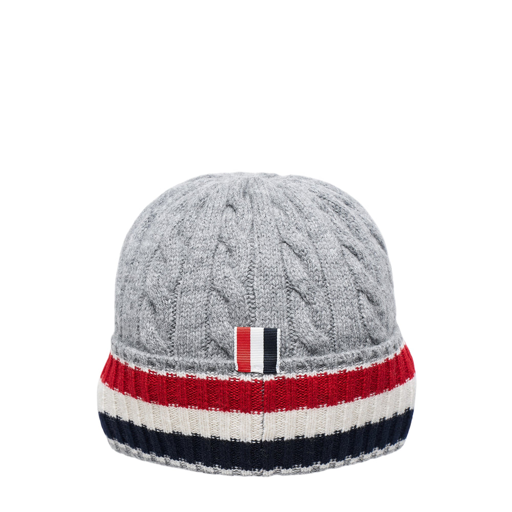 Thom Browne navy merino wool cable and rib knit beanie with signature red, white, and blue stripe detail and woven brand label at the brim, viewed from above