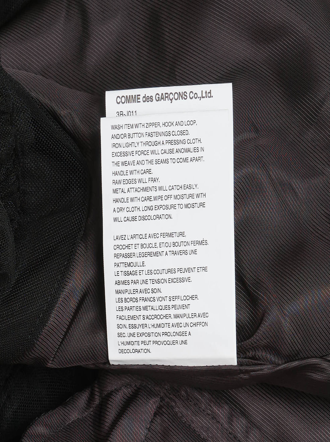 Noir Kei Ninomiya black oversized long sleeve jacket with high drawstring neck, silver zip closures, angled chest zip pockets, and layered black tulle ruffle hem, displayed flat on a white background - view 4