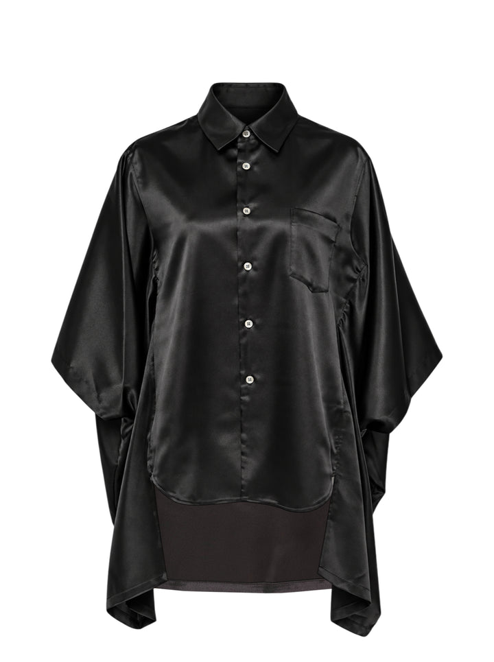 Comme des Garçons black polyester satin blouse with wide cape sleeves, button-front fastening, chest pocket, and contrast matte hem panel, displayed flat on a white background