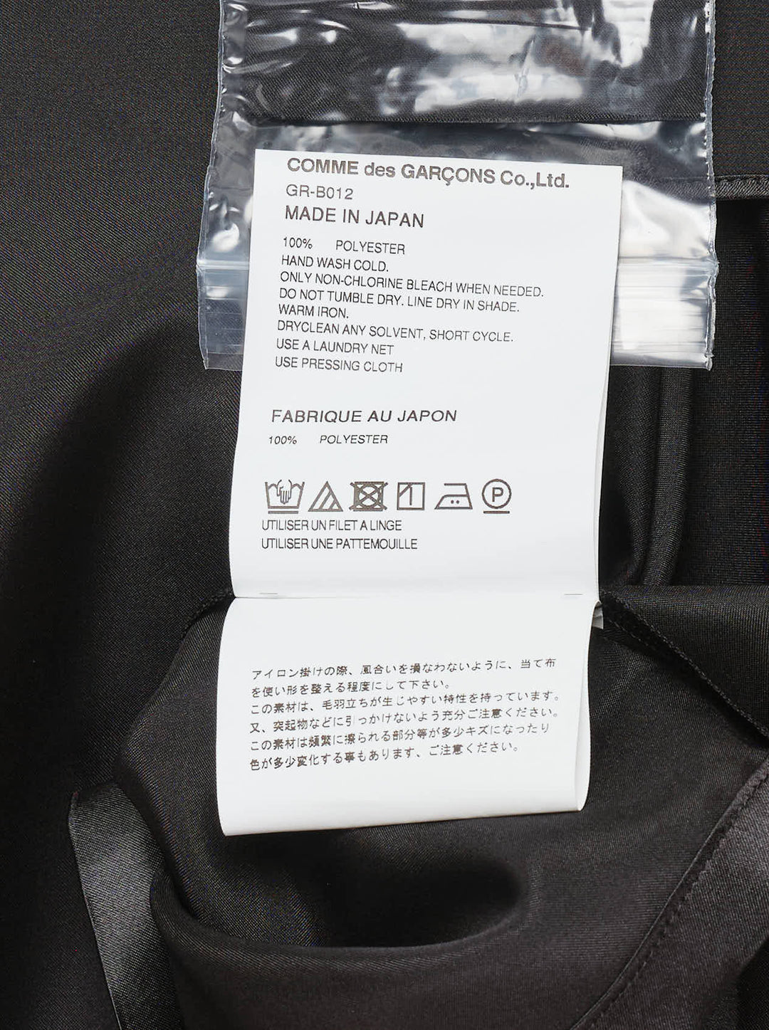 Comme des Garçons black polyester satin blouse with wide cape sleeves, button-front fastening, chest pocket, and contrast matte hem panel, displayed flat on a white background - view 4