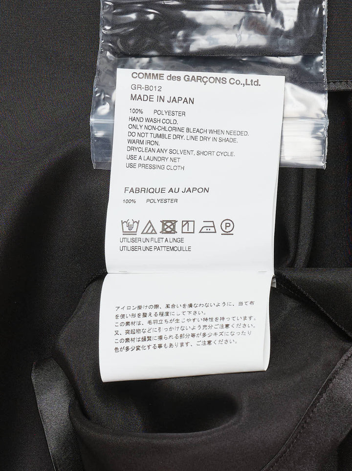 Comme des Garçons black polyester satin blouse with wide cape sleeves, button-front fastening, chest pocket, and contrast matte hem panel, displayed flat on a white background - view 4
