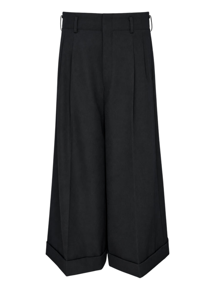 Comme des Garçons black wide leg pleated trousers with high waist, double front pleats, and deep turned-up cuffs, photographed flat on a white background