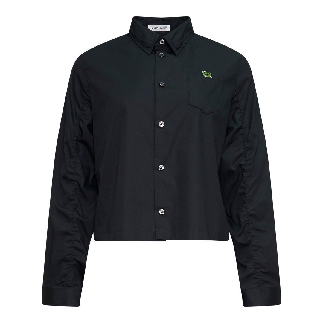 Undercover Cropped U Logo Blouse in black with gathered sleeves, point collar, tonal buttons, and a green embroidered Undercover logo on the chest pocket