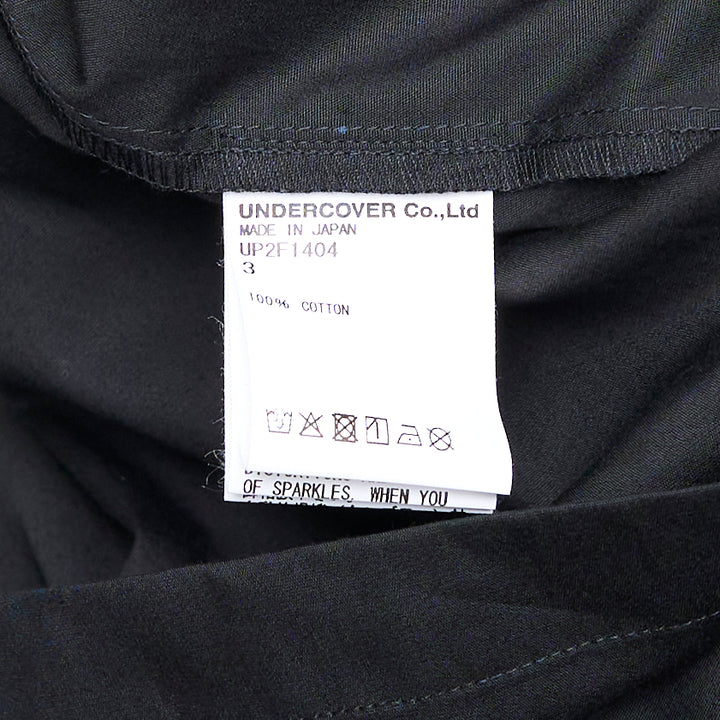 Undercover Cropped U Logo Blouse in black with gathered sleeves, point collar, tonal buttons, and a green embroidered Undercover logo on the chest pocket