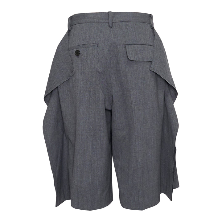Undercover grey wool-blend tailored shorts with oversized draped side flaps revealing navy lining, featuring belt loops, pleated front, and concealed zip fly