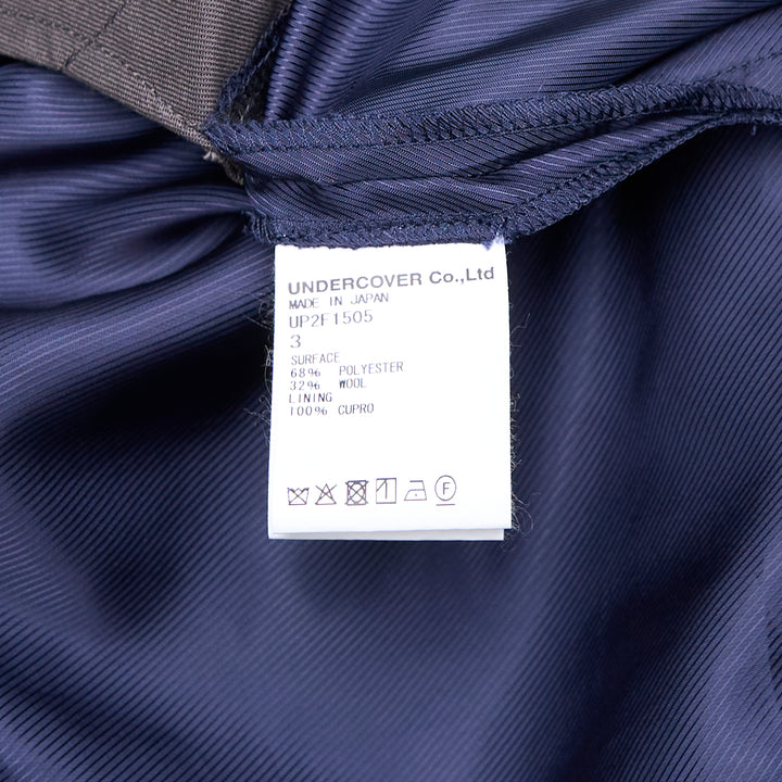 Undercover grey wool-blend tailored shorts with oversized draped side flaps revealing navy lining, featuring belt loops, pleated front, and concealed zip fly