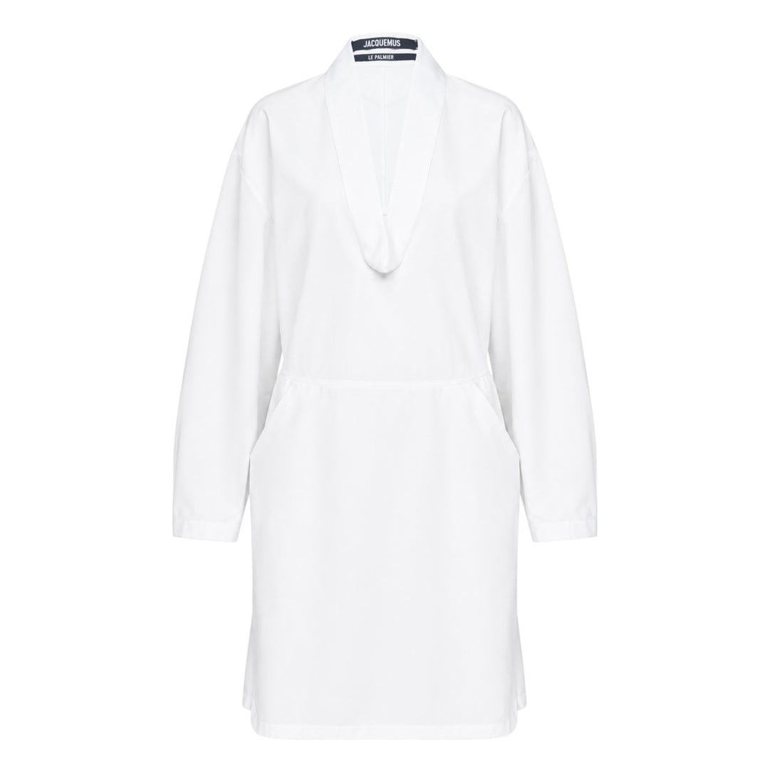 Jacquemus La Robe Colombe white long-sleeve mini dress with deep V-neckline, elasticated waist, front patch pocket, and navy logo tape at the back collar