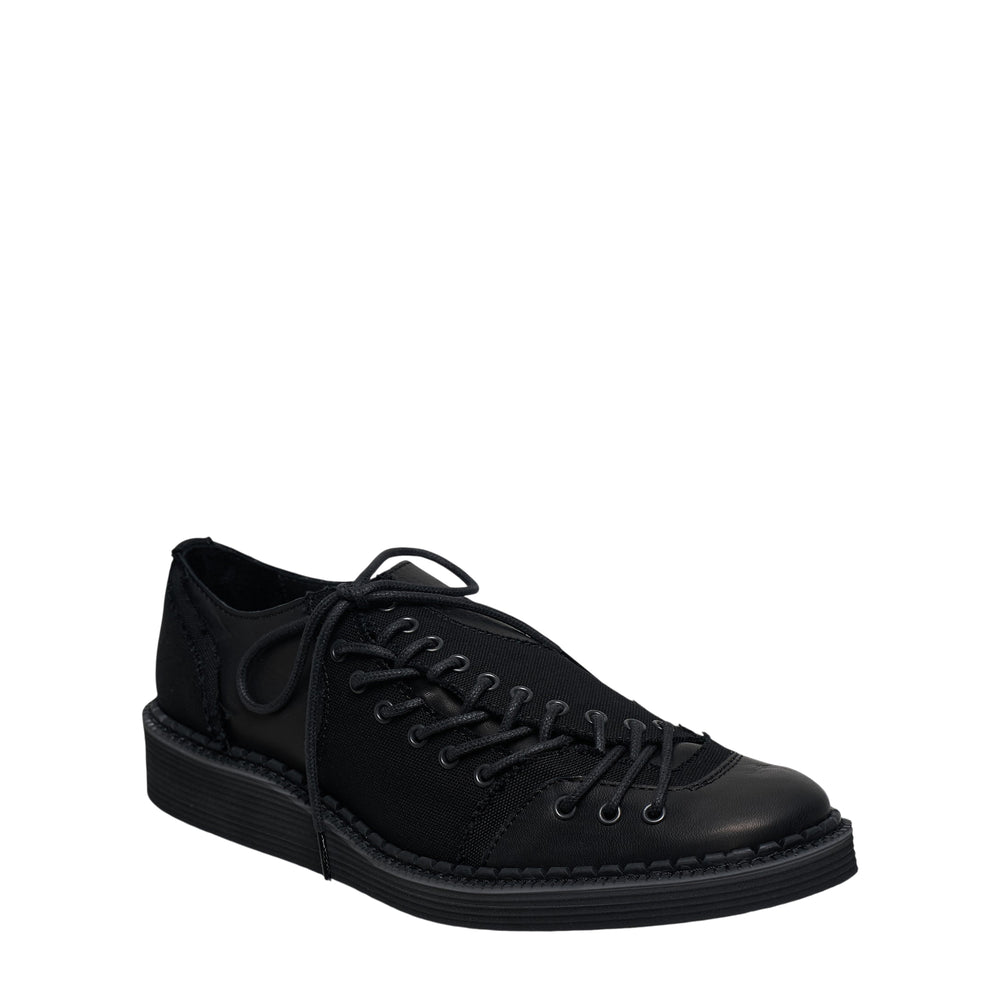Yohji Yamamoto Side Lace-Up Low Sneakers in all-black canvas and leather with exposed side lacing, metal eyelets, and a stacked ridged rubber sole, shown in profile view